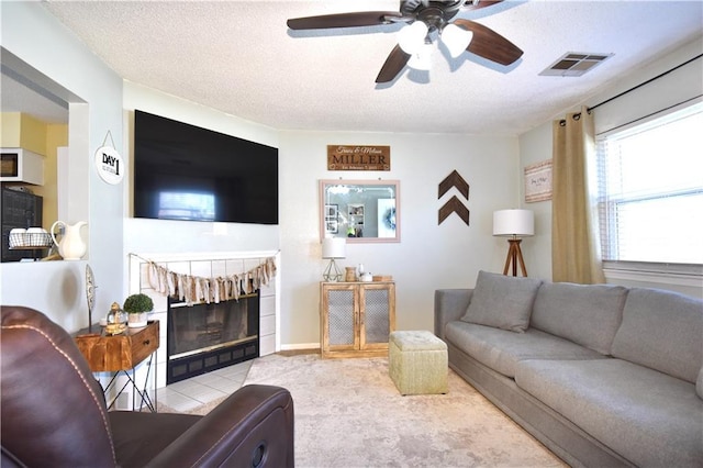 living area with ceiling fan, a textured ceiling, visible vents, and a tile fireplace