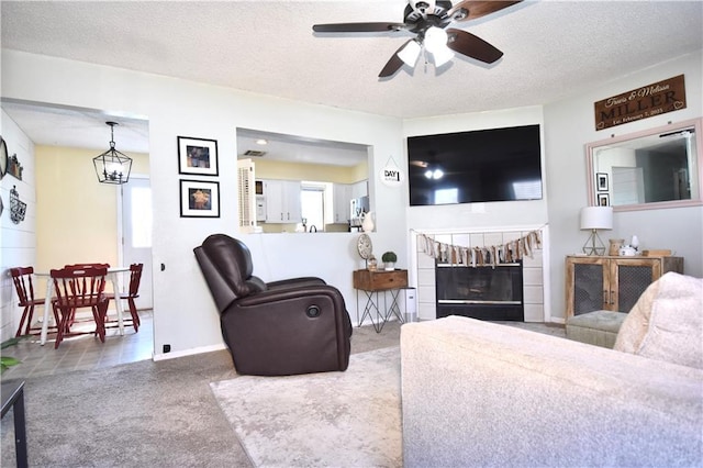 carpeted living area featuring ceiling fan, a fireplace, baseboards, and a textured ceiling