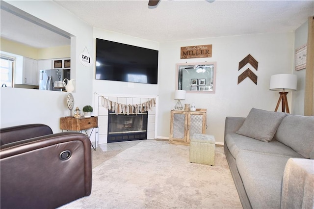 carpeted living room with a textured ceiling, baseboards, a tile fireplace, and ceiling fan