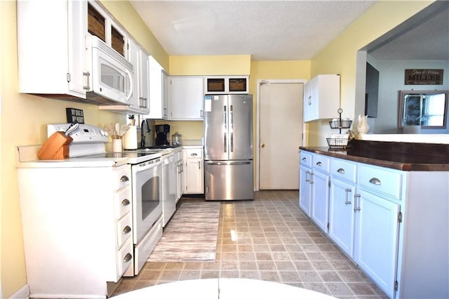 kitchen featuring dark countertops, white cabinets, white appliances, a textured ceiling, and a sink