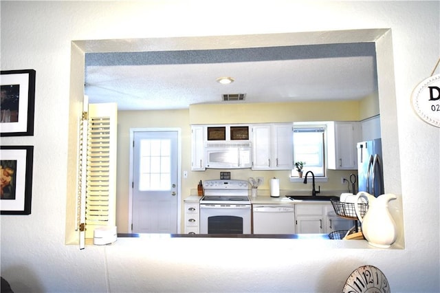 kitchen with visible vents, white cabinets, white appliances, a textured ceiling, and a sink