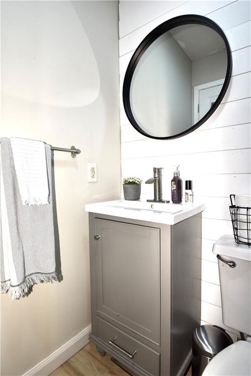 bathroom featuring baseboards, toilet, wood finished floors, and vanity