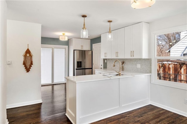 kitchen with stainless steel fridge with ice dispenser, dark wood-style flooring, a sink, light countertops, and tasteful backsplash