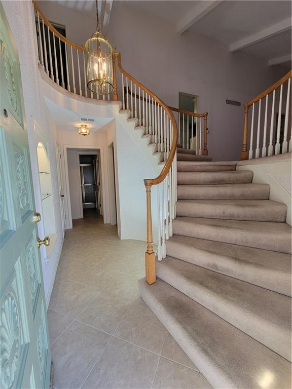 entrance foyer with visible vents, a chandelier, stairs, beam ceiling, and light tile patterned floors