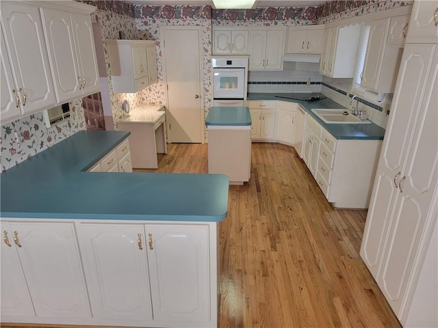 kitchen featuring oven, light wood-style flooring, a sink, white cabinets, and wallpapered walls