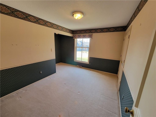 empty room with a textured ceiling, visible vents, wallpapered walls, wainscoting, and carpet flooring