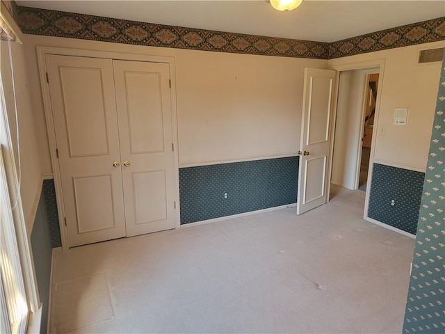 spare room with visible vents, light carpet, wainscoting, and wallpapered walls