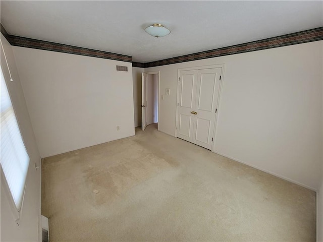 unfurnished bedroom featuring ornamental molding, visible vents, a closet, and light carpet