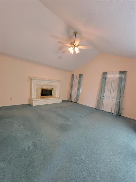 unfurnished living room with a high end fireplace, ceiling fan, carpet flooring, and vaulted ceiling