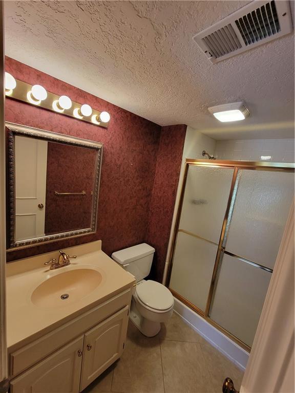 full bathroom featuring visible vents, a shower stall, toilet, tile patterned floors, and a textured ceiling