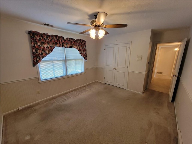 unfurnished bedroom featuring visible vents, carpet flooring, a closet, and wainscoting