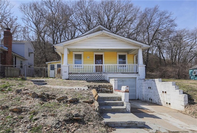 bungalow-style house featuring a garage, covered porch, concrete driveway, and fence