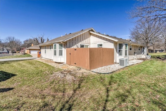 back of property with board and batten siding, fence, a lawn, and central AC