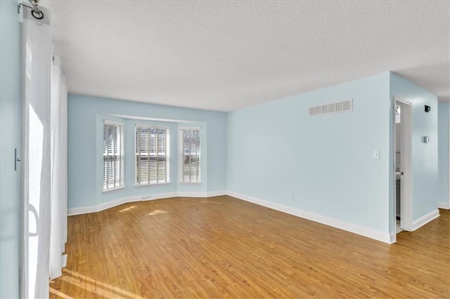 unfurnished room with visible vents, a textured ceiling, baseboards, and wood finished floors