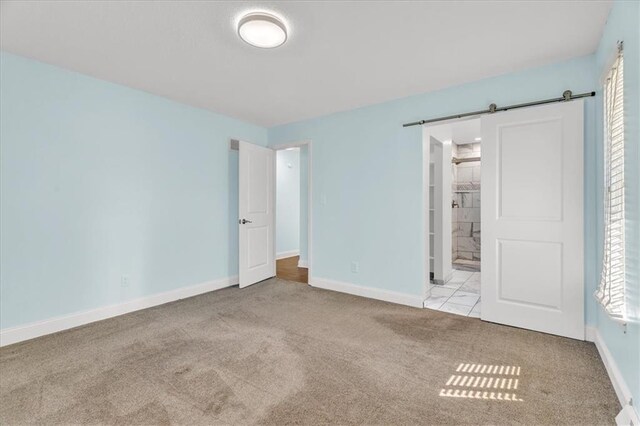 unfurnished bedroom featuring a barn door, baseboards, carpet, and ensuite bathroom