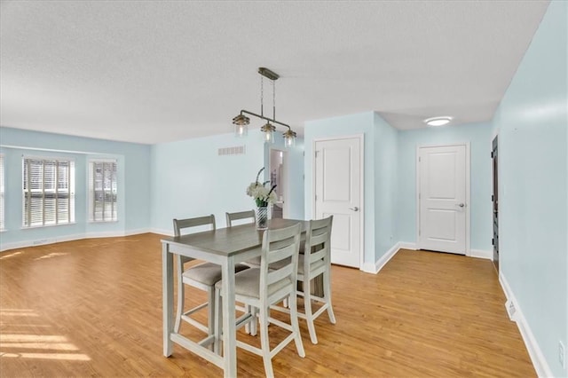 dining room with light wood-type flooring, baseboards, a textured ceiling, and visible vents