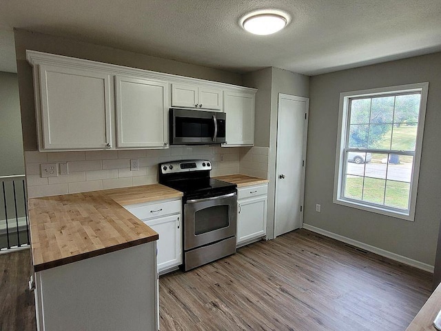 kitchen with wood counters, tasteful backsplash, white cabinetry, and stainless steel appliances