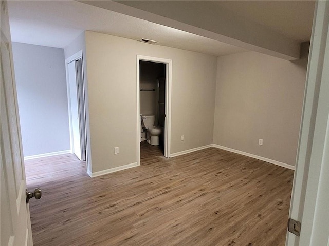 unfurnished bedroom featuring visible vents, ensuite bath, baseboards, and wood finished floors