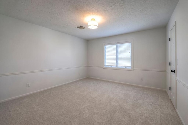 unfurnished room with a textured ceiling, light colored carpet, visible vents, and baseboards