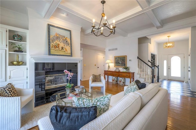 living area featuring a tiled fireplace, beamed ceiling, visible vents, and a chandelier