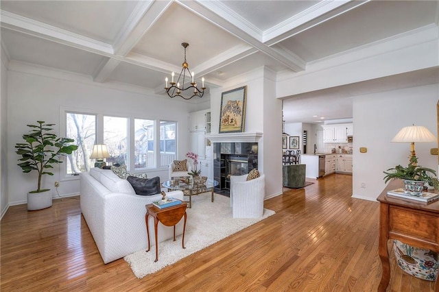 living area featuring beamed ceiling, light wood-type flooring, a tile fireplace, an inviting chandelier, and coffered ceiling