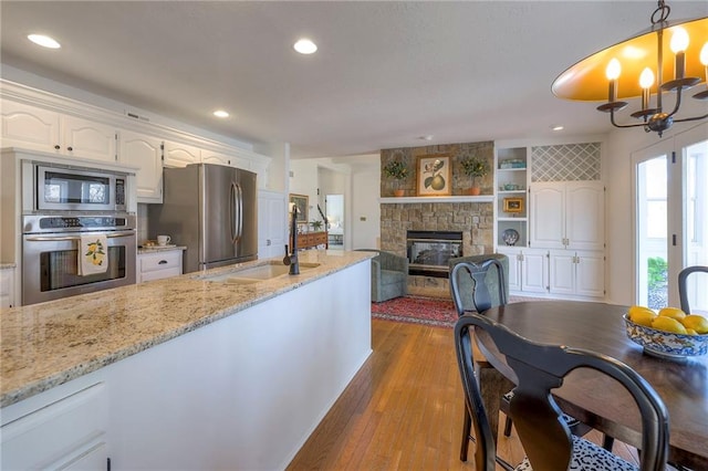 kitchen featuring a sink, wood finished floors, stainless steel appliances, white cabinets, and light stone countertops