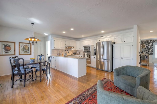 kitchen featuring light wood-style flooring, a sink, a peninsula, appliances with stainless steel finishes, and white cabinets