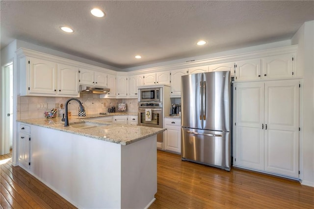 kitchen featuring under cabinet range hood, hardwood / wood-style floors, light stone counters, appliances with stainless steel finishes, and a peninsula