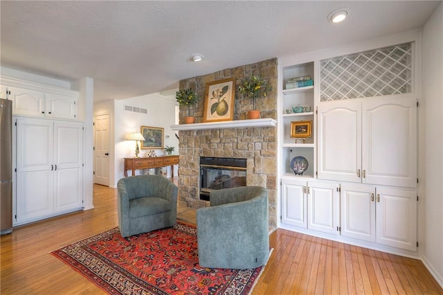 living room featuring a stone fireplace, built in features, light wood-style floors, and visible vents