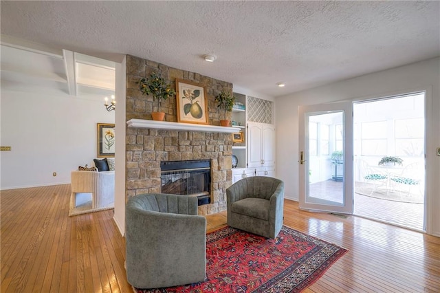 living room featuring baseboards, light wood finished floors, a stone fireplace, a textured ceiling, and beamed ceiling