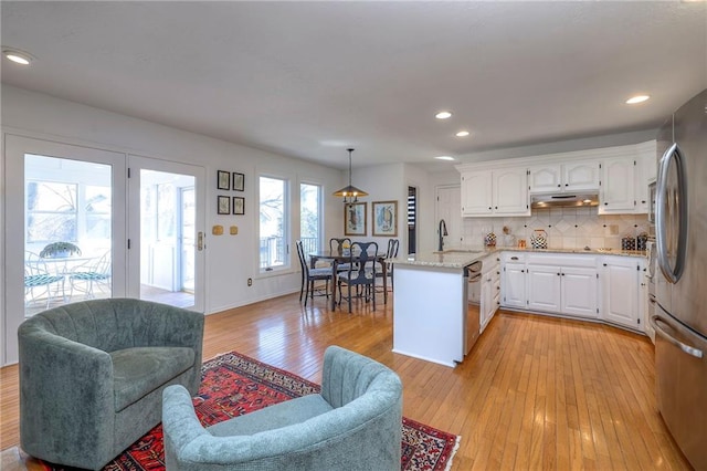 kitchen featuring light wood-style flooring, under cabinet range hood, a sink, stainless steel appliances, and a peninsula