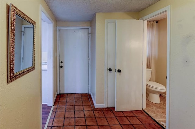 hall with tile patterned floors, baseboards, and a textured ceiling