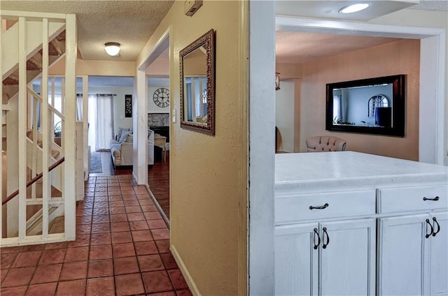 hallway with stairs, dark tile patterned floors, and a textured ceiling