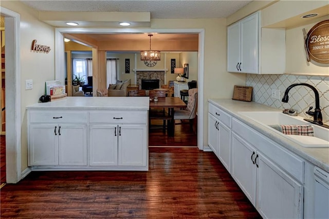 kitchen featuring dark wood finished floors, light countertops, a stone fireplace, white cabinetry, and a sink