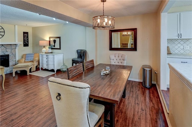 dining room featuring baseboards, a notable chandelier, dark wood-style floors, and a fireplace