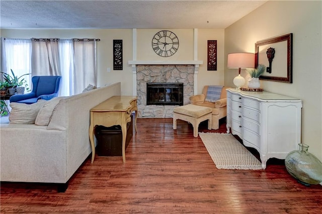 living area featuring a textured ceiling, a stone fireplace, and wood finished floors