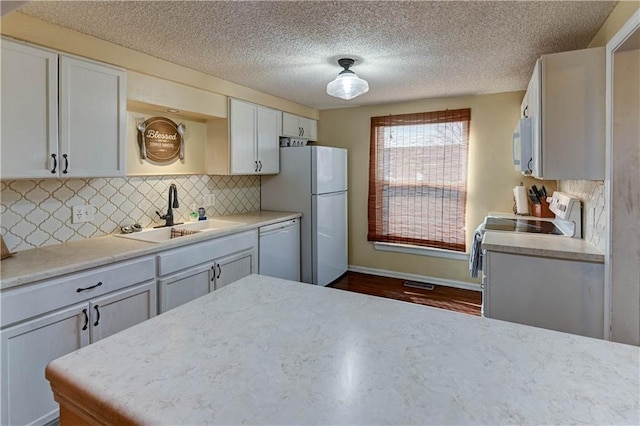 kitchen featuring backsplash, light countertops, white cabinets, white appliances, and a sink