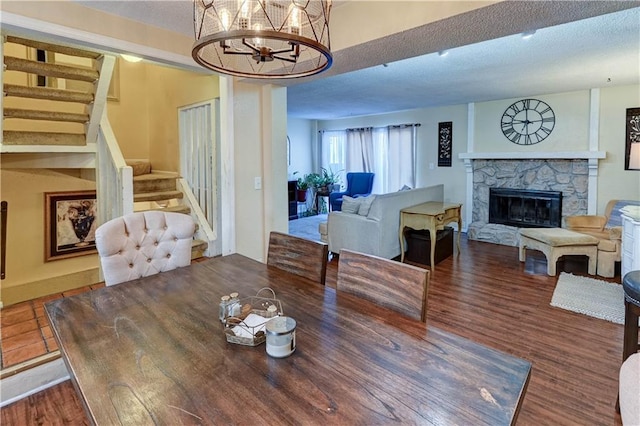 dining area featuring stairway, a stone fireplace, an inviting chandelier, wood finished floors, and a textured ceiling