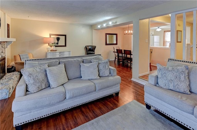 living area with baseboards, ceiling fan, a stone fireplace, wood finished floors, and a textured ceiling