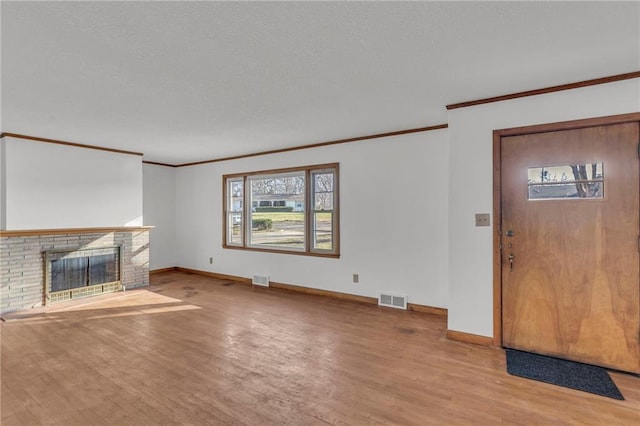 unfurnished living room with visible vents, a textured ceiling, wood finished floors, a fireplace, and crown molding