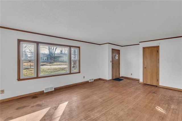 spare room with visible vents, light wood-style flooring, a textured ceiling, crown molding, and baseboards