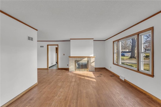 unfurnished living room featuring a brick fireplace, light wood-style floors, visible vents, and a textured ceiling