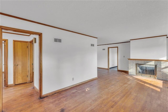 unfurnished living room featuring light wood-type flooring, visible vents, a textured ceiling, a fireplace, and crown molding