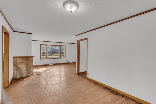 empty room featuring baseboards, visible vents, a textured ceiling, crown molding, and light wood-type flooring