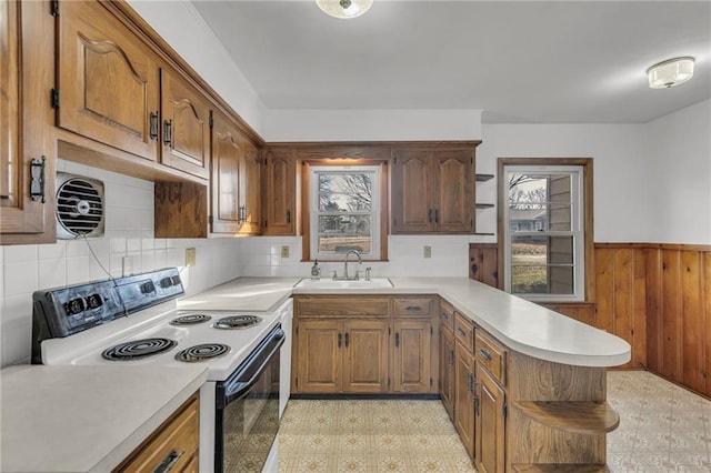 kitchen featuring a sink, range with electric stovetop, a peninsula, wainscoting, and light floors