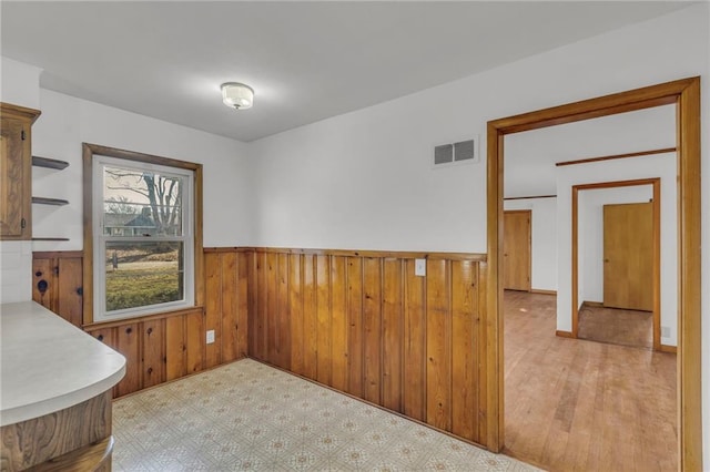 unfurnished dining area featuring wooden walls, visible vents, wainscoting, and light floors