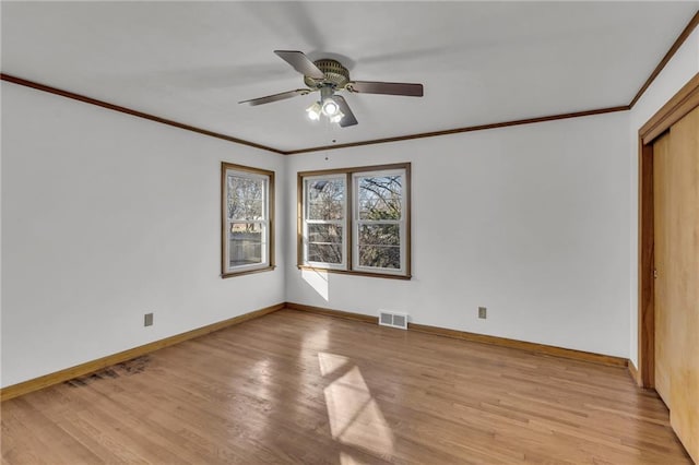 spare room with baseboards, visible vents, light wood finished floors, and ornamental molding