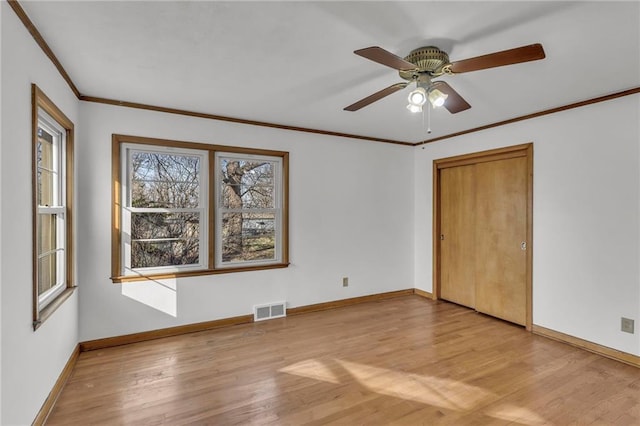 spare room featuring crown molding, light wood-style floors, visible vents, and baseboards