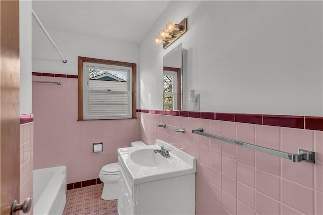 bathroom with tile walls, toilet, a tub to relax in, wainscoting, and vanity