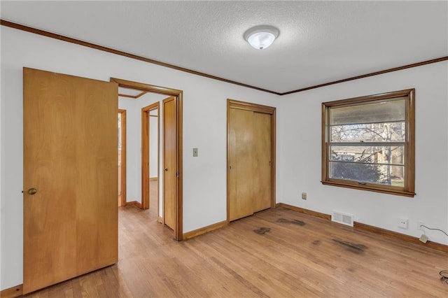 unfurnished bedroom with visible vents, ornamental molding, light wood-style floors, a closet, and a textured ceiling